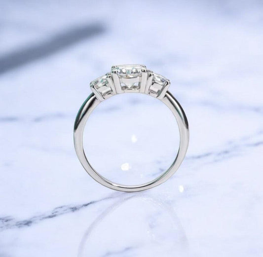 Moissanite engagement ring with 3 stone design, 1 carat main stone and 925 sterling silver, with D color and VVS clarity, on a marble countertop, made by russmoon