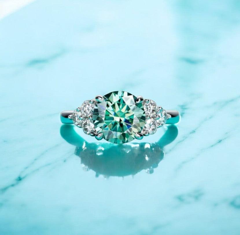 3 carat green moissanite engagement ring with VVS clarity displayed on a white marble countertop with a shadow behind it, made by russmoon