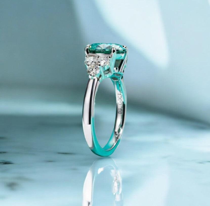 3 carat green moissanite engagement ring with VVS clarity displayed on a white marble countertop with a shadow behind it, made by russmoon