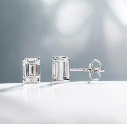 Emerald cut moissanite stud earrings displayed on a white marble counter with slight blue tones, made by russmoonco