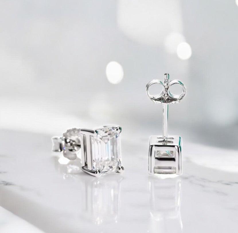 Emerald cut moissanite stud earrings displayed on a white marble counter with slight blue tones, made by russmoonco