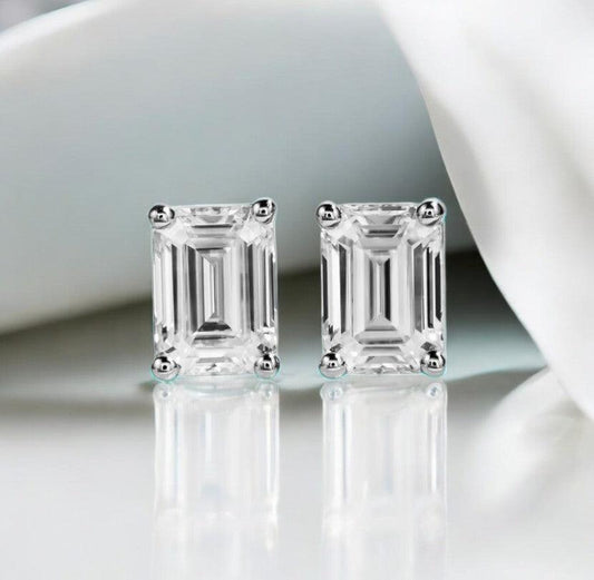 Emerald cut moissanite stud earrings displayed on a white marble counter with slight blue tones, made by russmoonco