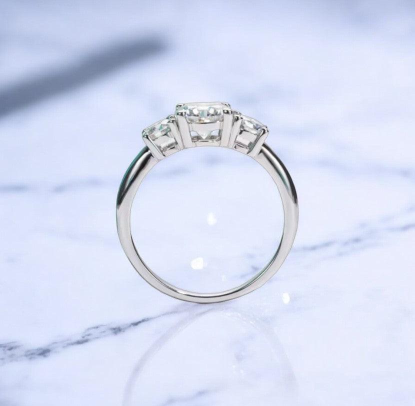 Moissanite engagement ring with 3 stone design, 1 carat main stone and 925 sterling silver, with D color and VVS clarity, on a marble countertop, made by russmoon