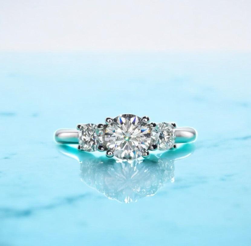 Moissanite engagement ring with 3 stone design, 1 carat main stone and 925 sterling silver, with D color and VVS clarity, on a marble countertop, made by russmoon