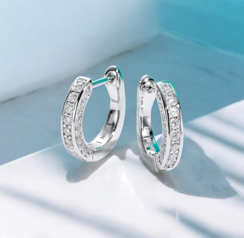 Moissanite hoop earrings with pave design, 925 sterling silver, displayed on a white marble counter, with light blue tones in the background, made by russmonco
