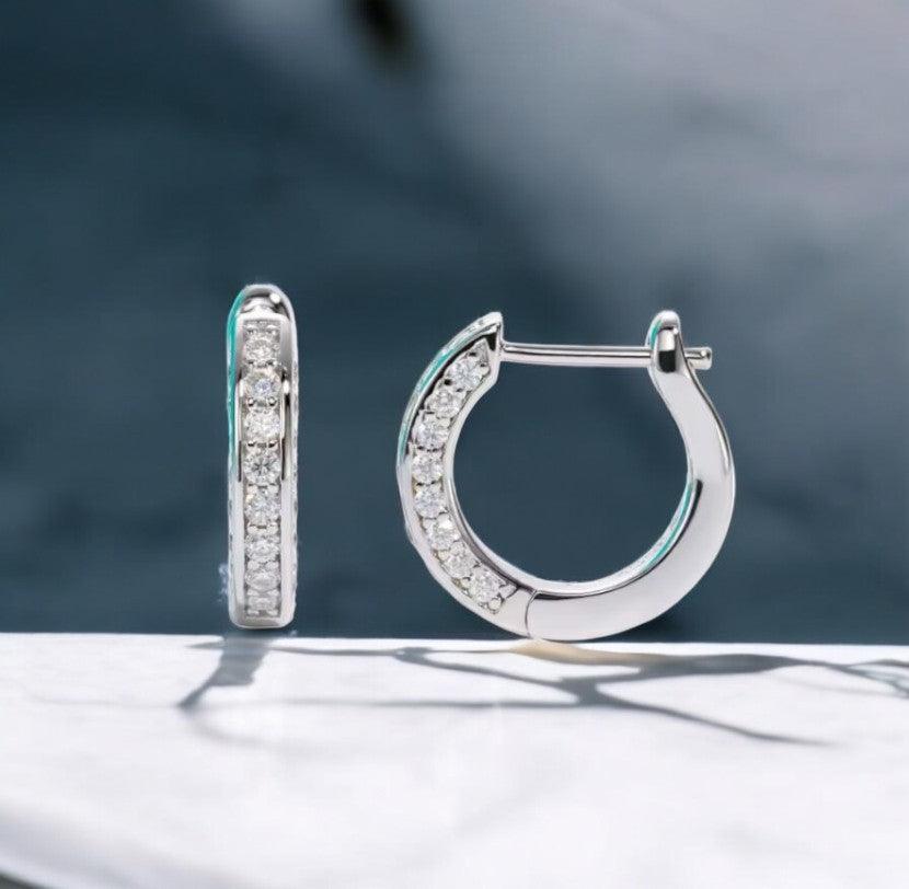 Moissanite hoop earrings with pave design, 925 sterling silver, displayed on a white marble counter, with light blue tones in the background, made by russmonco
