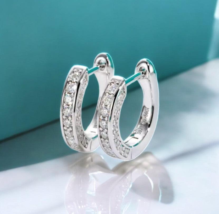 Moissanite hoop earrings with pave design, 925 sterling silver, displayed on a white marble counter, with light blue tones in the background, made by russmonco
